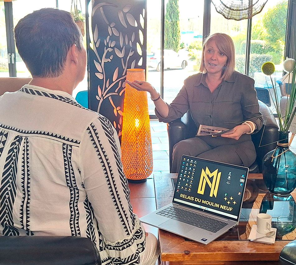 Entretien dans le lounge du Relais du Moulin Neuf pour préparer un séminaire, ordinateur avec logo et brochures sur la table